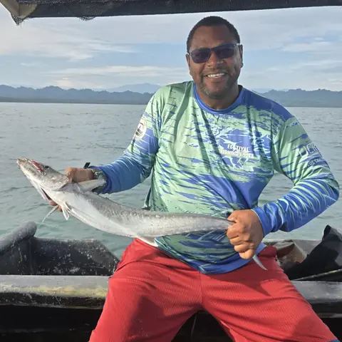 Holding up a fresh-caught mackerel on the boat, with mountains across the water